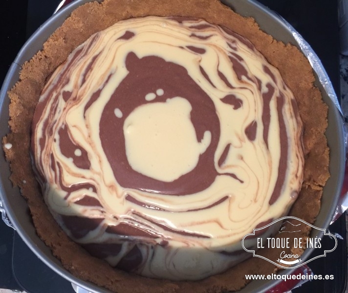 Y ahora sacamos el molde con la galleta de la nevera y vamos alternado a echar las dos mezclas por encima con cuidado, podemos usar al final una brocheta o un tenedor para entremezclar si queremos algo más los dos colores.