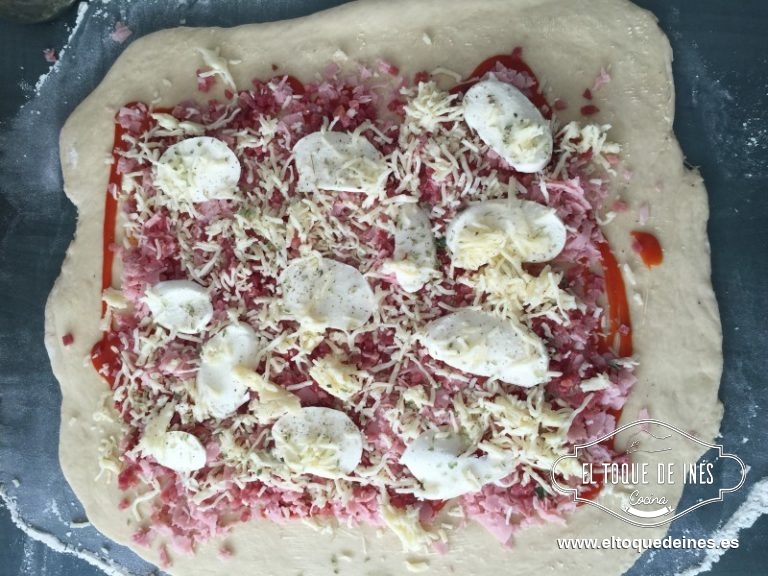 Cubrimos la masa con el tomate, encima el jamón York en lonchas o picado, encima el jamón serrano en taquitos extendido bien por toda la masa , cortamos la bola de mozzarella en lonchas y la repartimos ,sobre todo esto espolvoreamos la que tenemos rallada y repartimos la pimienta y el orégano.