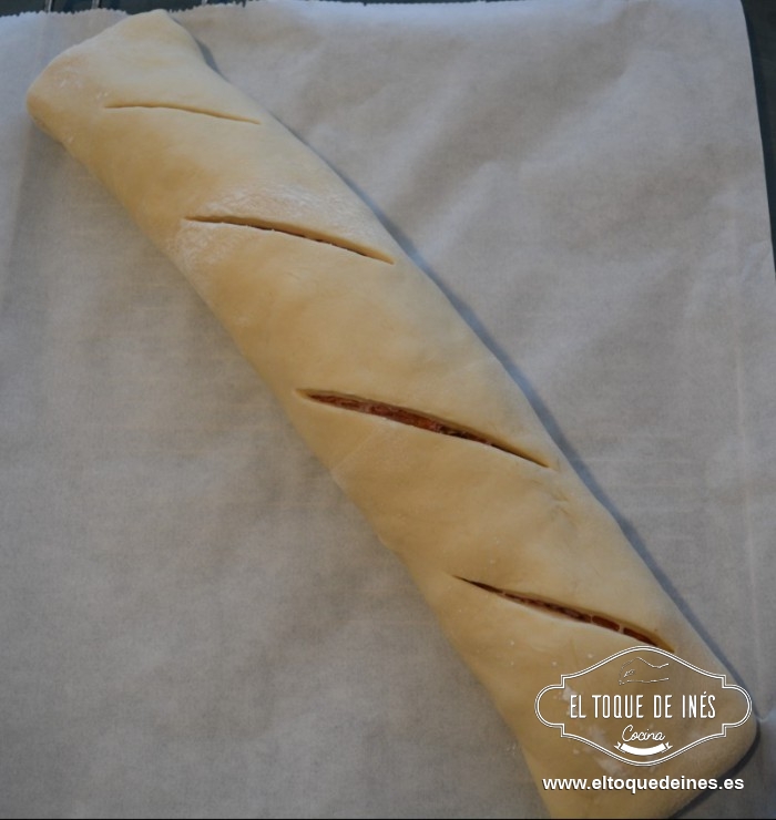 Humedecemos con agua uno de los bordes de la masa y comenzamos a enrollar como si fuese un brazo de gitano apretando bien ,terminando en la zona humedecida para sellarlo bien. Cerramos las puntas hacia abajo para que no se nos abra.