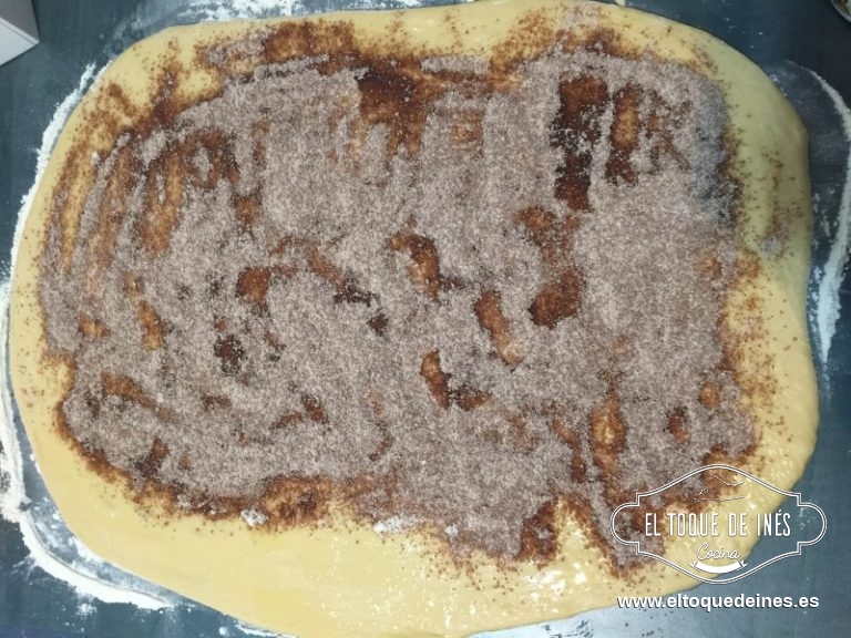 Pintamos la superficie con la mantequilla derretida, espolvoreamos la mezcla que tenemos reservada por encima excepto por uno de los extremos para poder pegar bien la masa sin que se nos abra.