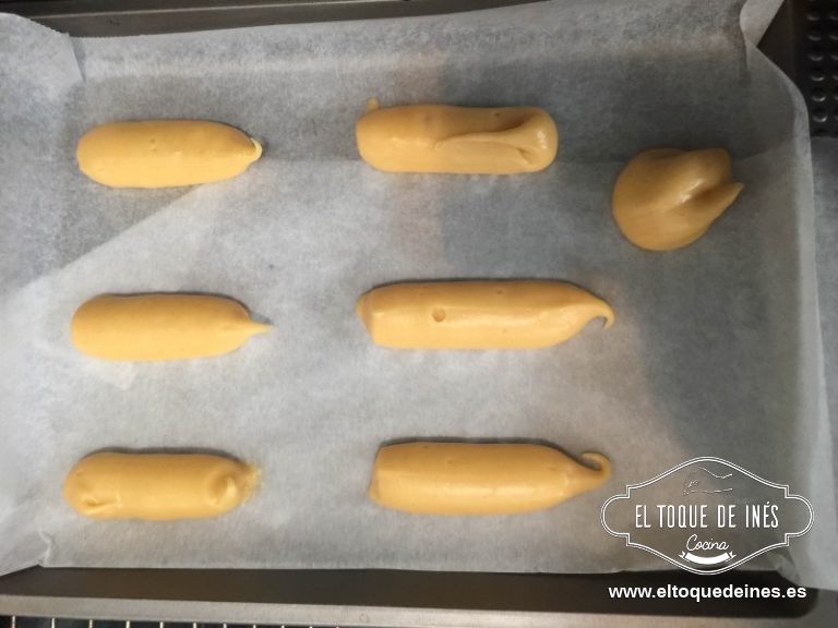 Rellenamos una manga pastelera con la masa y sobre un papel de horno hacemos formas alargadas como de 5-6 cm.