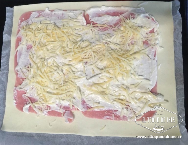 Colocamos sobre la masa el jamón de york, encima la mezcla de quesos, encima de eso el queso en lonchas (opcional) y espolvoreamos queso rallado.