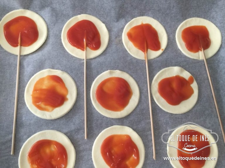Ponemos sobre papel de horno uno de los círculos, colocamos el palito, echamos el tomate frito, encima la verdura y el lacón o lo que vosotros hayáis decidido como relleno y espolvorear con un poquitín de queso rallado.