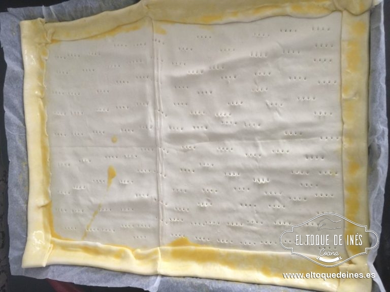 Estiramos la plancha del hojaldre , le doblamos el borde todo y lo pegamos bien; pinchamos toda la base bien para que no suba luego en el horno. Pintamos todo el borde con huevo batido; la base no la pintéis porque sino se cerrarán los agujerillos y se os subirá el hojaldre.