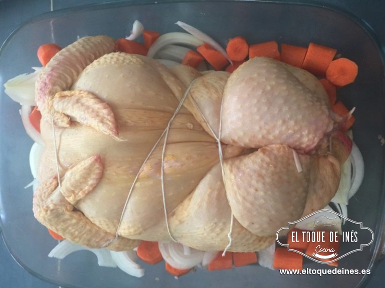 En una fuente de horno echamos la cebolla en rodajas, las zanahorias en trozos y colocamos el pollo encima.