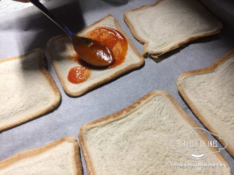 Colocamos sobre papel de horno, echando una cucharada de tomate frito sobre cada una de las 4 rebanadas.