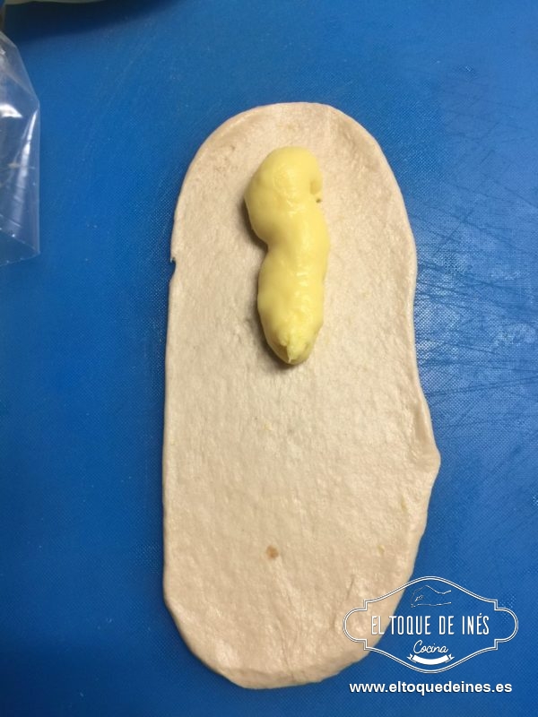 Estiramos cada bolita de masa, colocamos crema pastelera dentro en un extremo.
