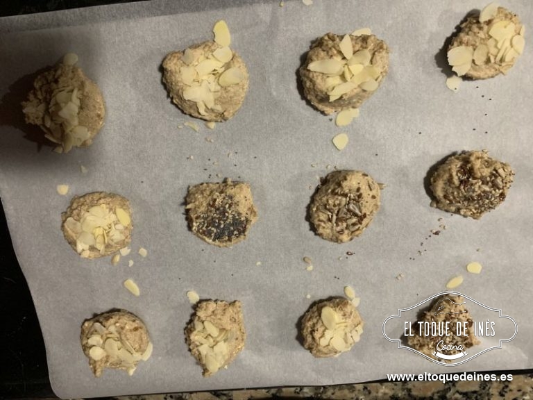Vamos colocando las bolitas sobre papel sulfurizado de horno y las aplastamos un poco según le vamos poniendo las semillas o la almendra laminada, así se quedan pegadas a la superficie.