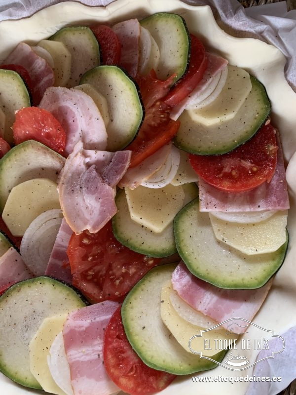 Vamos colocando superponiendo un poco una rodaja de calabacín, patata, cebolla, bacon y tomate.