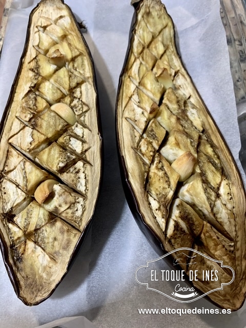 Cortamos al medio la berenjena, le hacemos unos cortes en la carne y metemos los dientes de ajo en medio cortados.