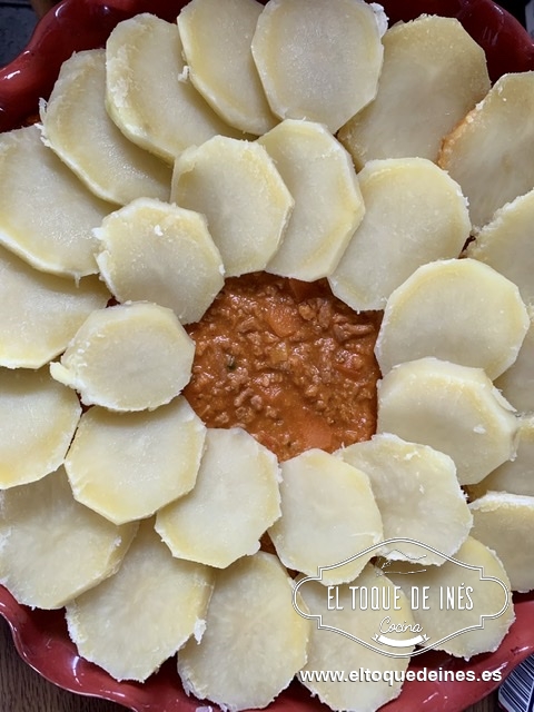 En una fuente de horno echamos la carne que ya tenemos preparada y encima vamos situando las patatas que se superpongan un poco unas encima de otras.